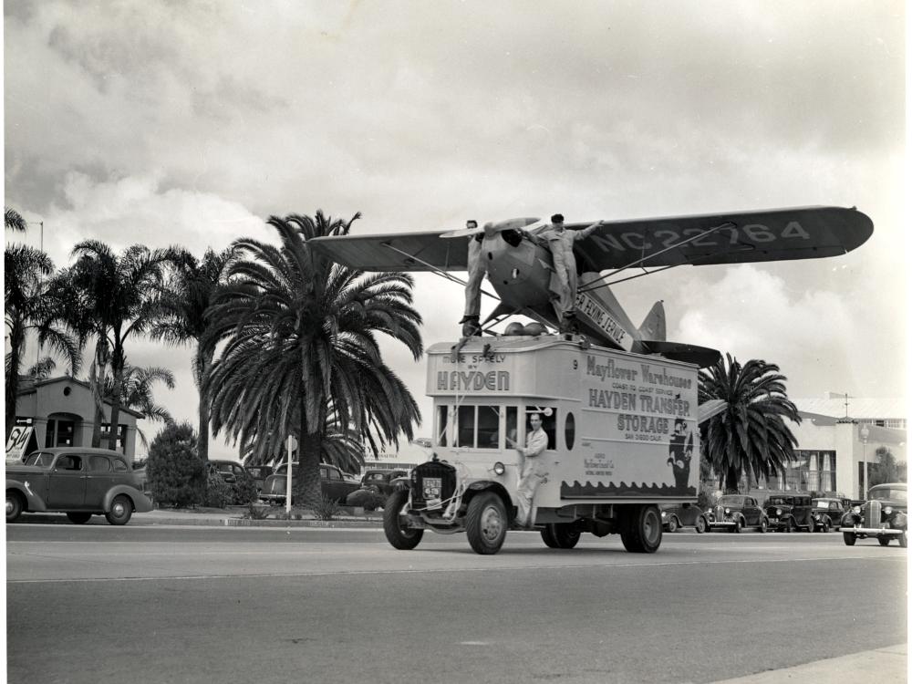 A Piper Cub J-4A, a monoplane with one engine, is displayed on a truck as part of an advertisement.