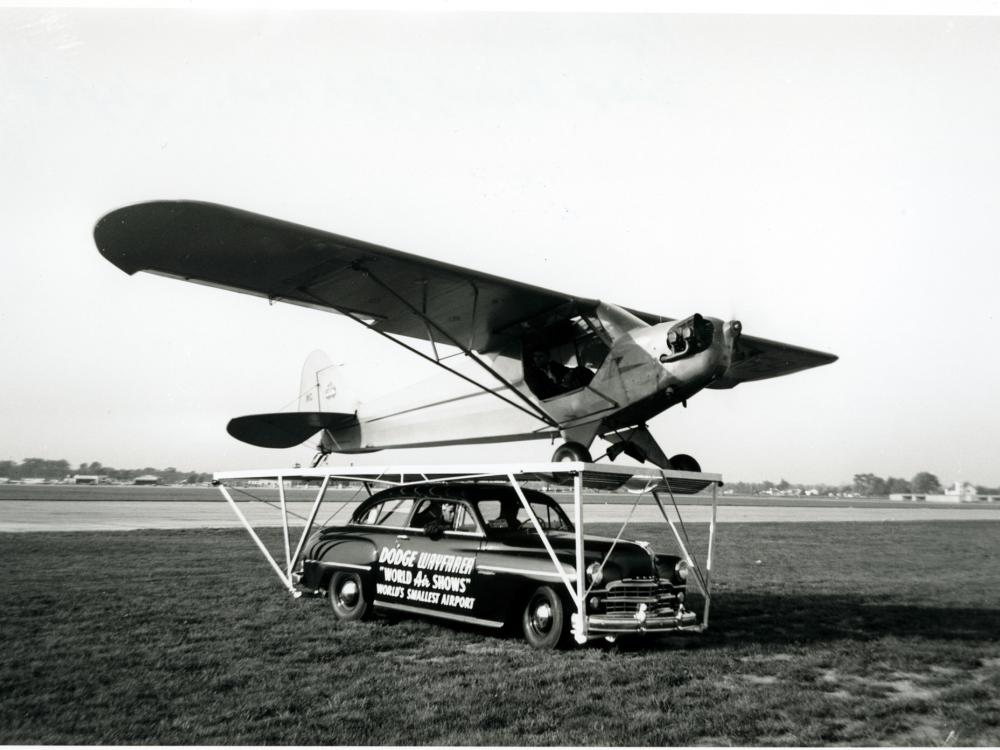 A Piper Cub, a monoplane with one engine, is placed on top of a car prior to performing a stunt.