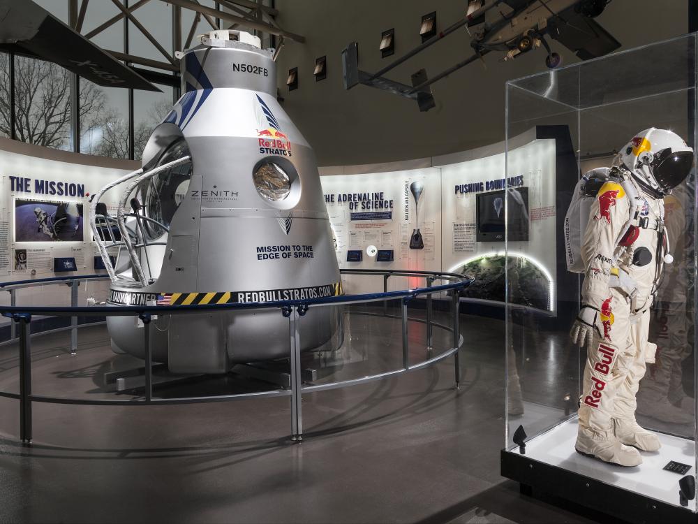 Side view of an exhibit about a Red Bull-sponsored free falling mission from the edge of space. A high-altitude pressure suit is seen in front of the silver-colored opened capsule used to freefall.