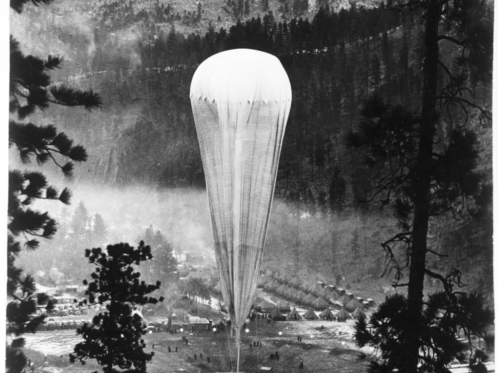 A tall air balloon sits on land in a forest clearing.