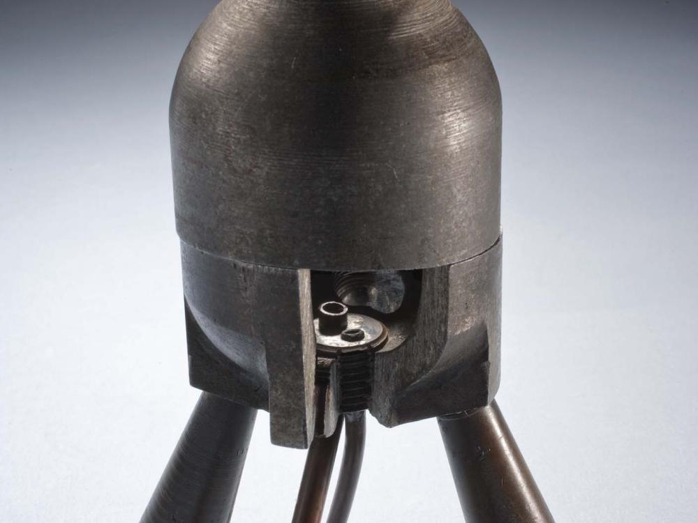 Metal rocket motor with four leg-like tubes below a cylinder-shaped combustion chamber. Small cutaway revealing the interior of the chamber.