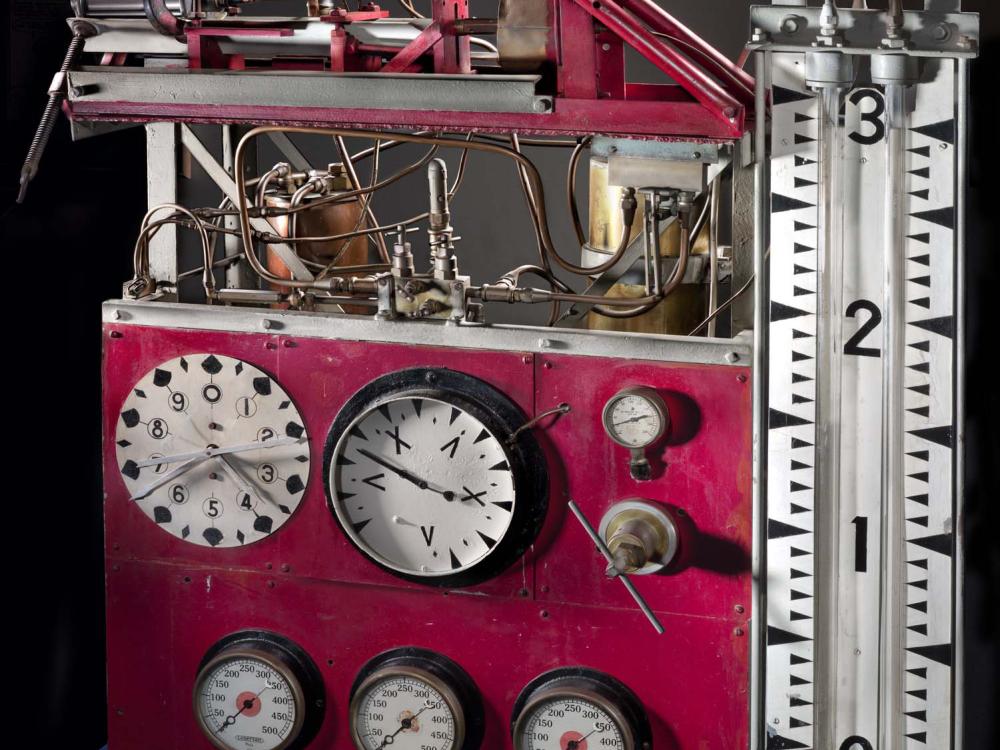 Large table stand with multiple clock-like meters and a large pressure meter. Above the meters are a two-story set of tubes.