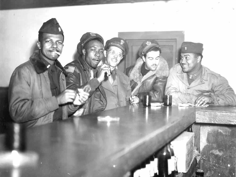 A group of Tuskegee Airmen sit and enjoy drinks and conversation at a bar.