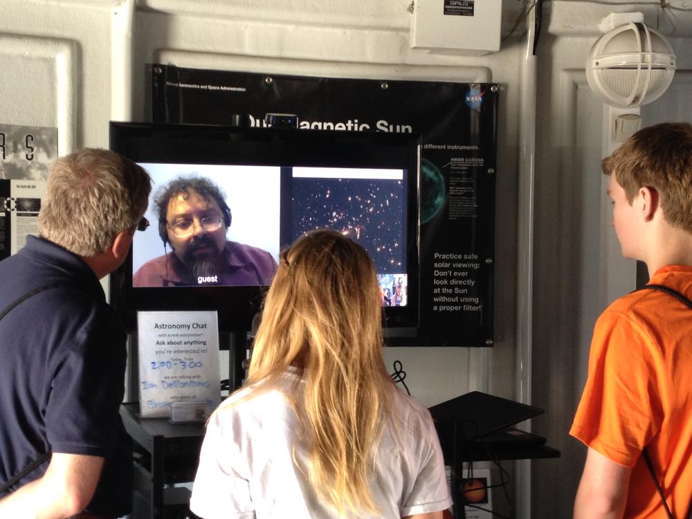 Three museum visitors speak with a male expert on astronomy on video chat at the Museum's public observatory.