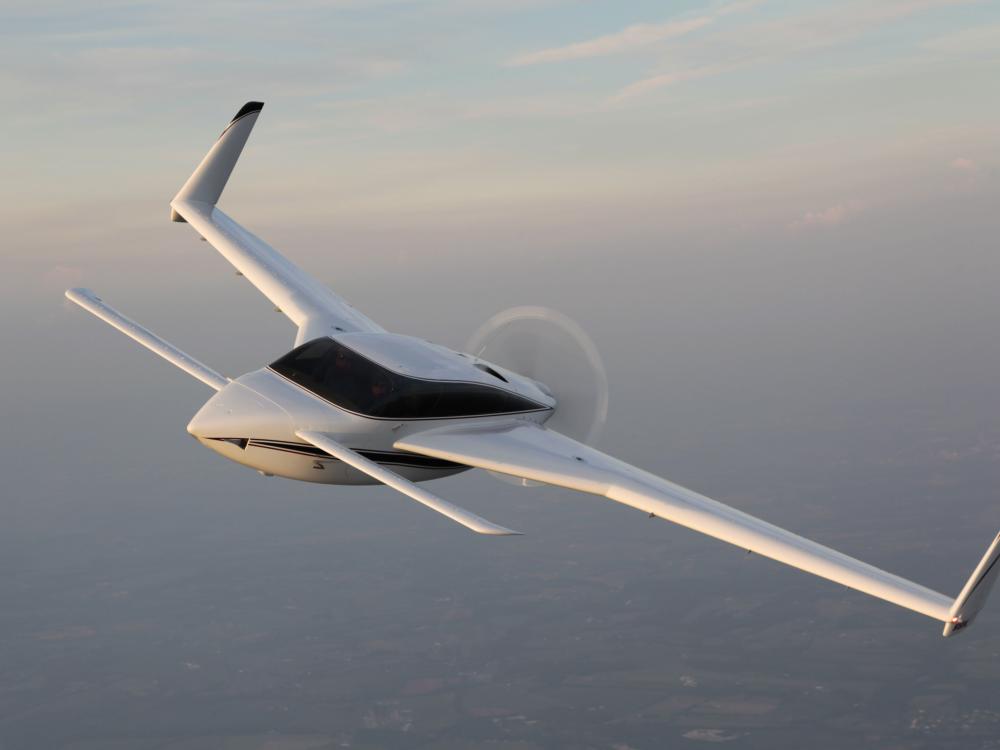 View of white monoplane in flight with long wings that feature fins on the ends of the wings.