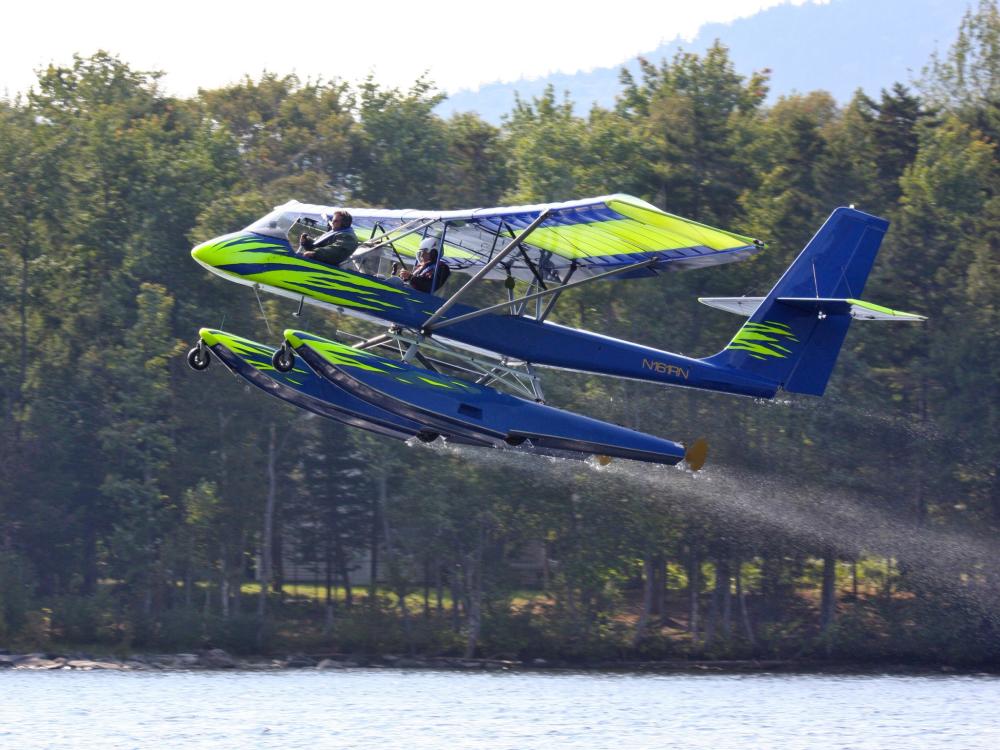 Side view of blue and green seaplane with pontoon floats below fuselage.