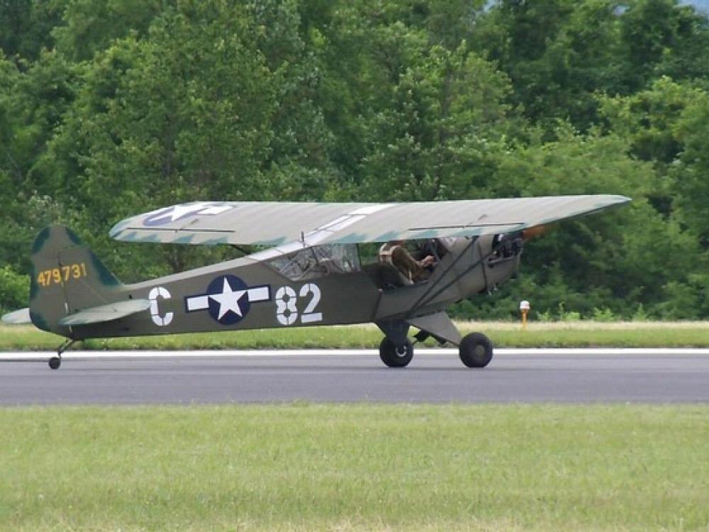 Side view of gray and green military monoplane with one engine.The letter "C" and number "82" are painted in white paint on the sides of a blue and white star emblem.