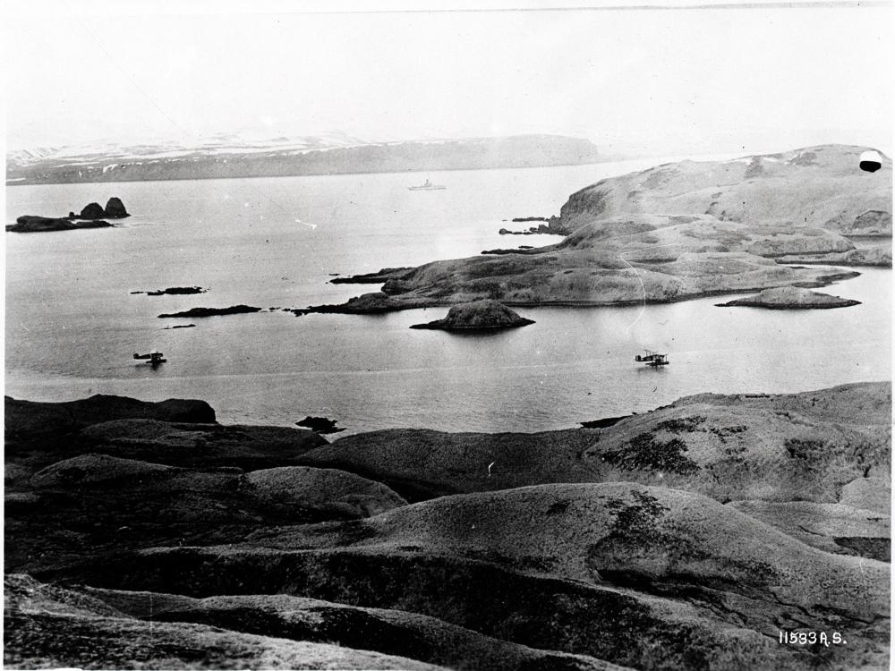 Two aircraft fly directly over a large body of water.