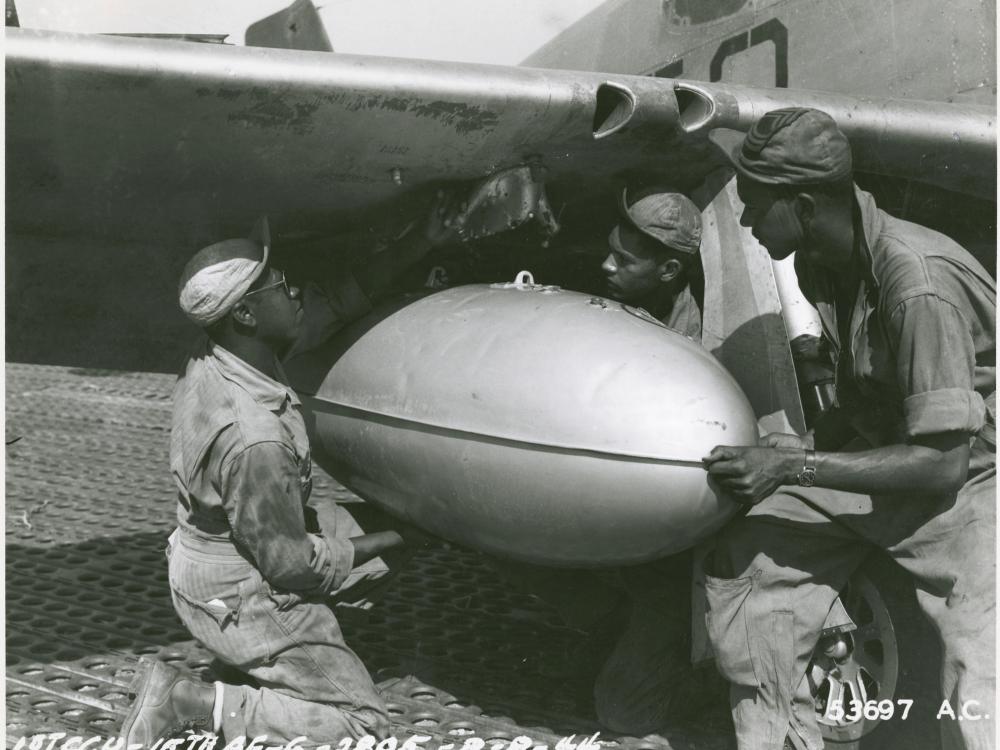 Members of a ground crew for a U.S. fighter group install a fuel tank onto the wing of a fighter plane.