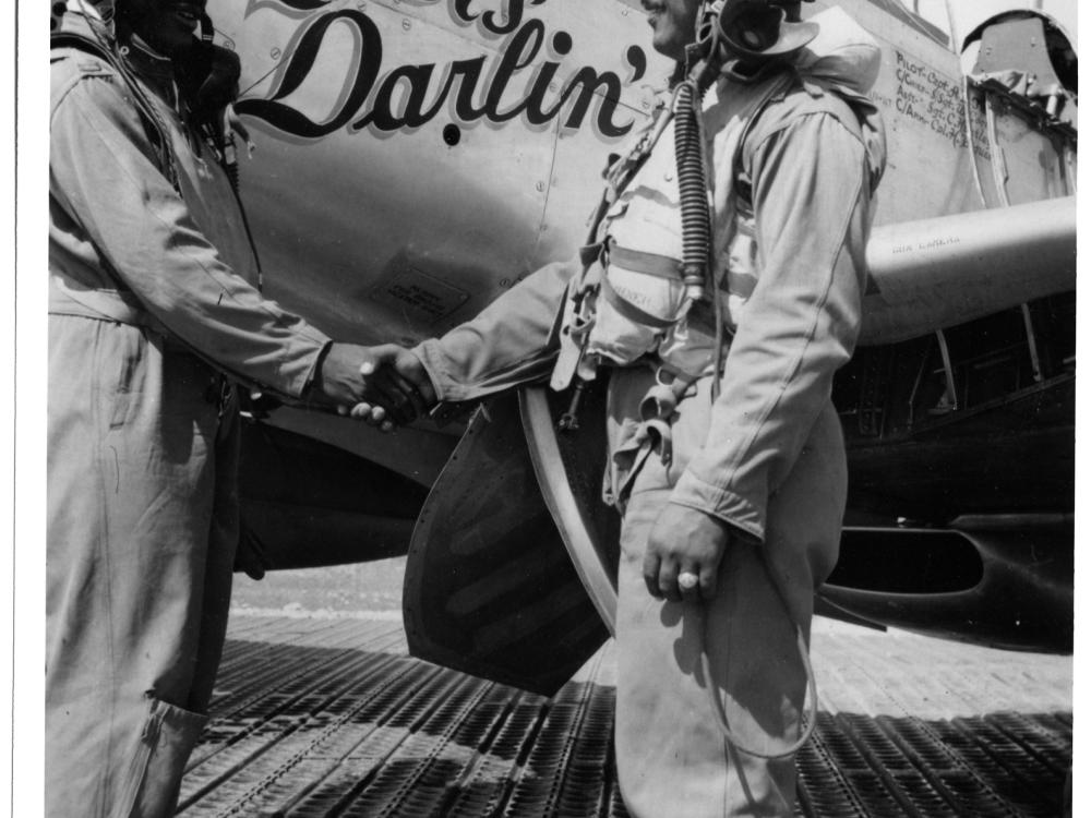 Clarence D. “Lucky” Lester and Andrew D. Turner, both of whom are African-American male pilots, shake each other's hand in front of an aircraft.