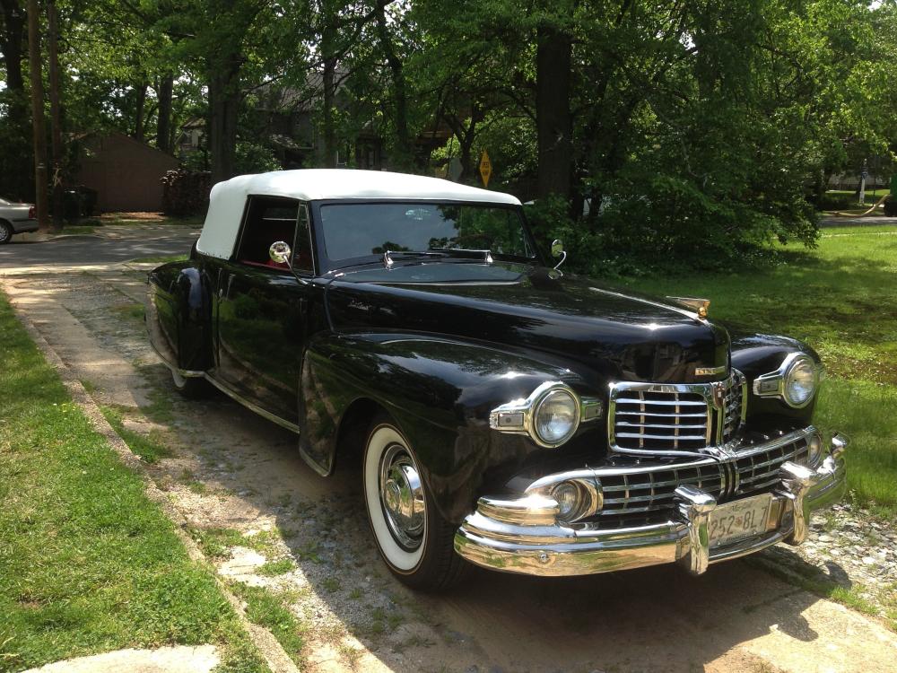 Diagonal front view of a black, two-door antique automobile with a white retractable roof.