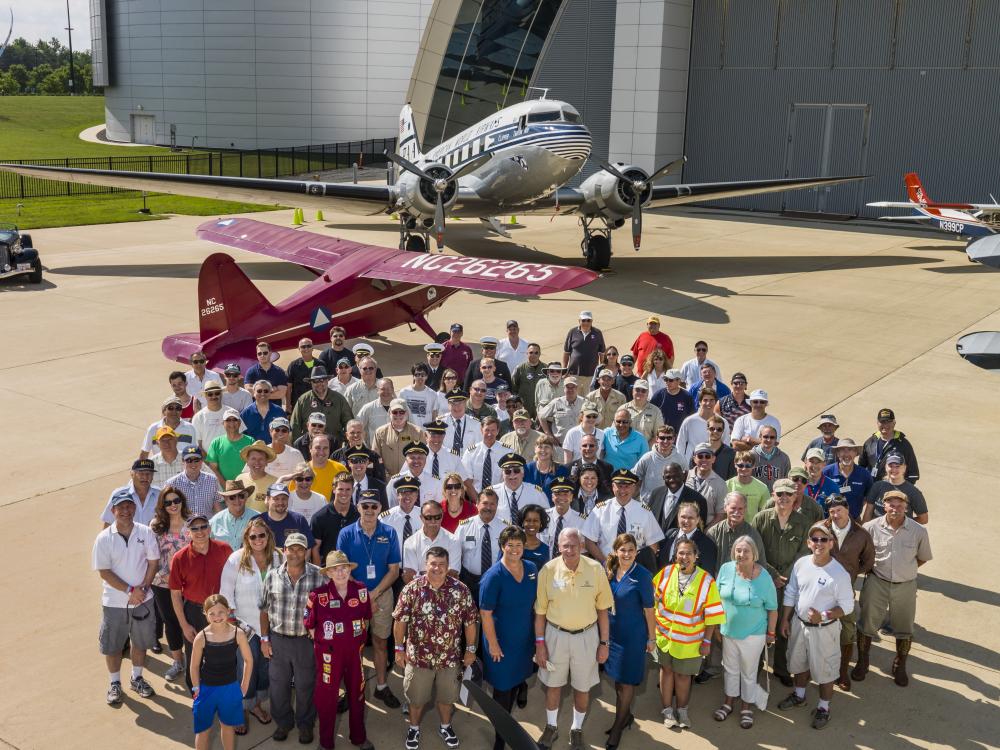 A group of pilots and crew members who participated in a pilot event at the Museum stand together with a former director of the Museum for a group photo.