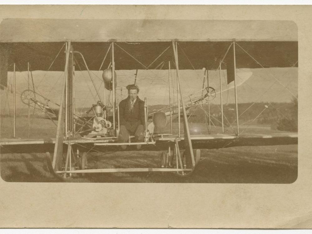 Harry Bingham Brown, a white male, sits at the cockpit of a Wright biplane.