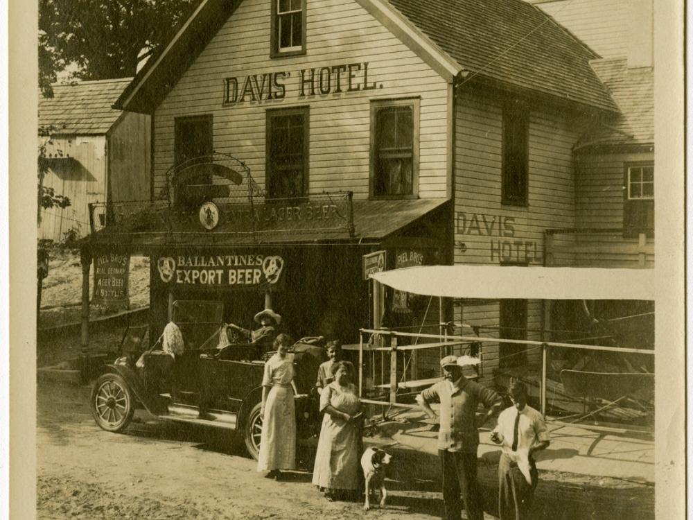 Harry Bingham Brown, a white male pilot, stands outside of a hotel named "Davis' Hotel" with other people.