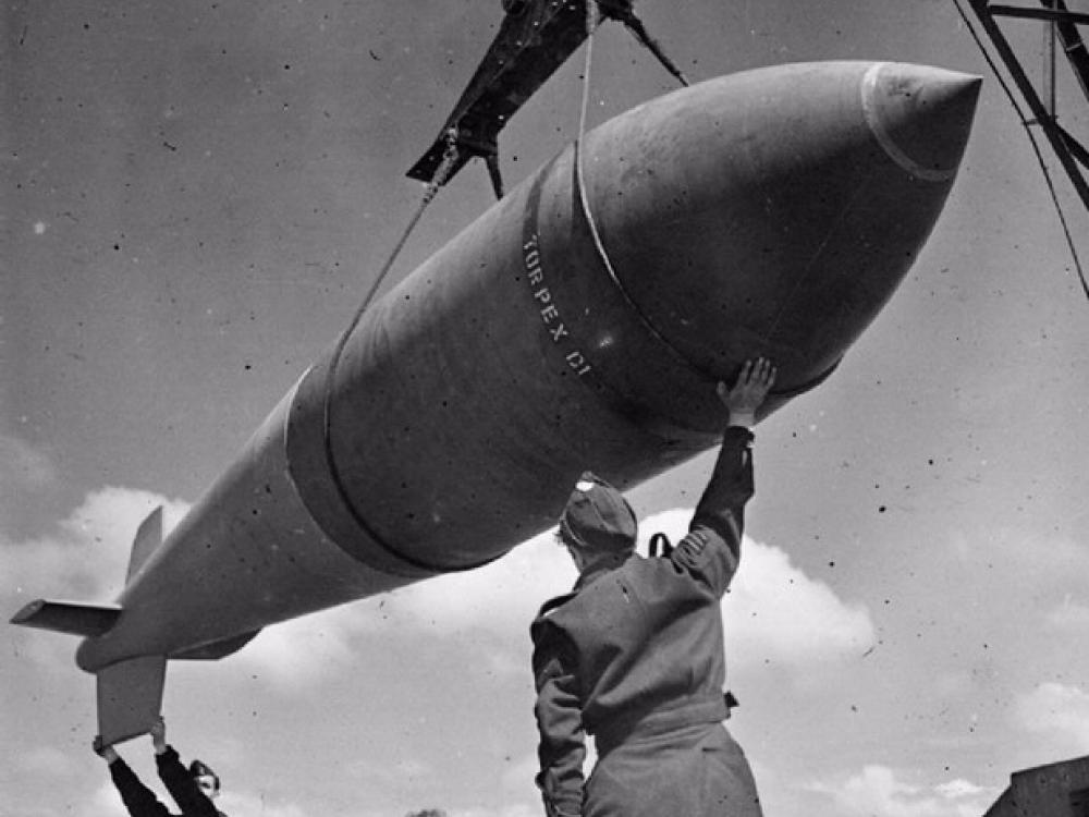 Two men assist in hoisting a large bomb shaped like a missile.