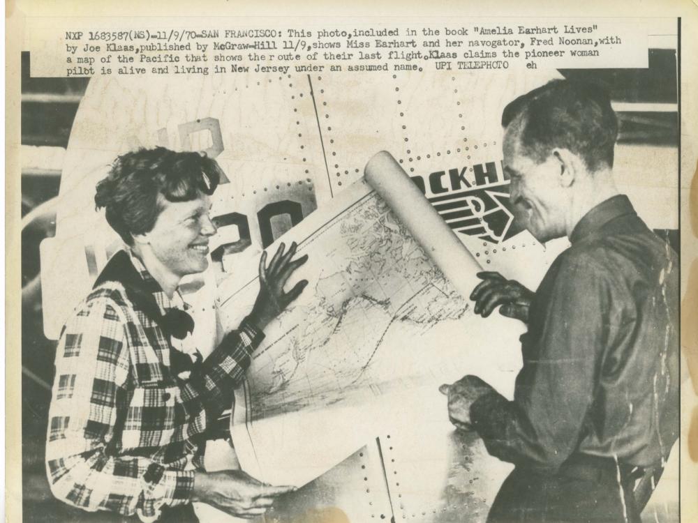 Amelia Earhart, a white female pilot, and Fred Noonan, a white male navigator, stand together looking at a map. A caption suggests a different ending to the flight that led to Earhart's disappearance.