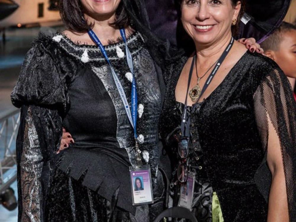 Two women wearing Halloween costumes pose behind a dish of candy at the Museum's annual Halloween event.