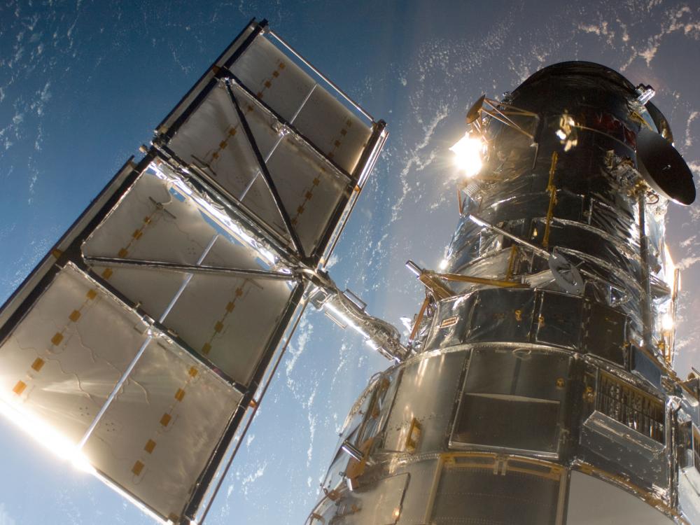 Partial view of the Hubble Space Telescope, a large telescope with two sets of solar panels (one on each side), from the perspective of the Space Shuttle Atlantis.