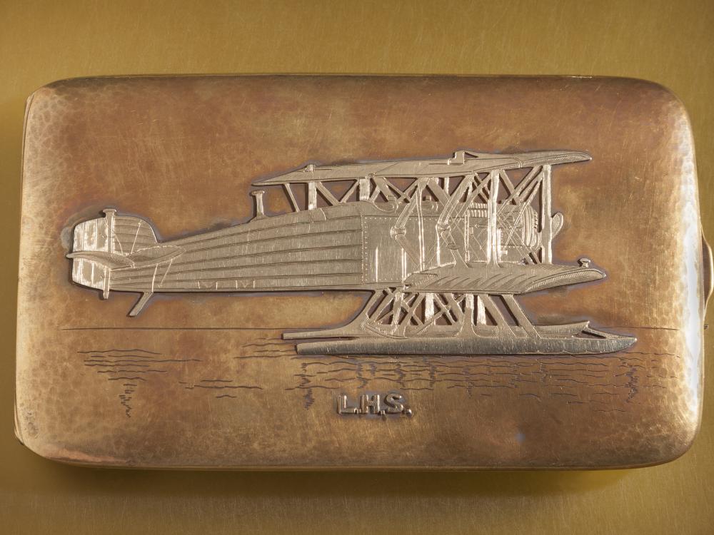 Top of golden box-shaped case featuring an engraved golden biplane.