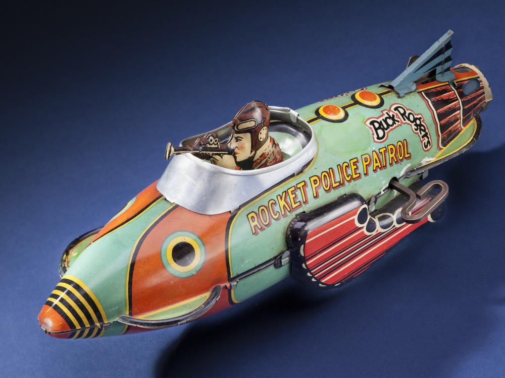 Side view of light green and orange rocket ship figure with character figure in cockpit. "Rocket Police Patrol" is painted on the side of the cockpit in yellow and black.