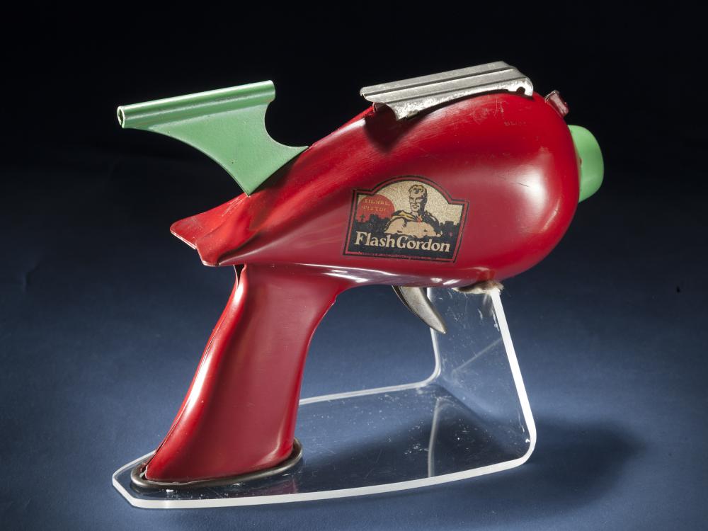 Side view of red-colored steel gun toy with light green trigger. Flash Gordon logo on the middle of the toy.