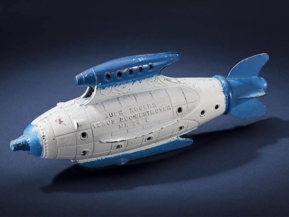 Side view of white torpedo-shaped destroyer toy with blue propellor, nose, and fins.