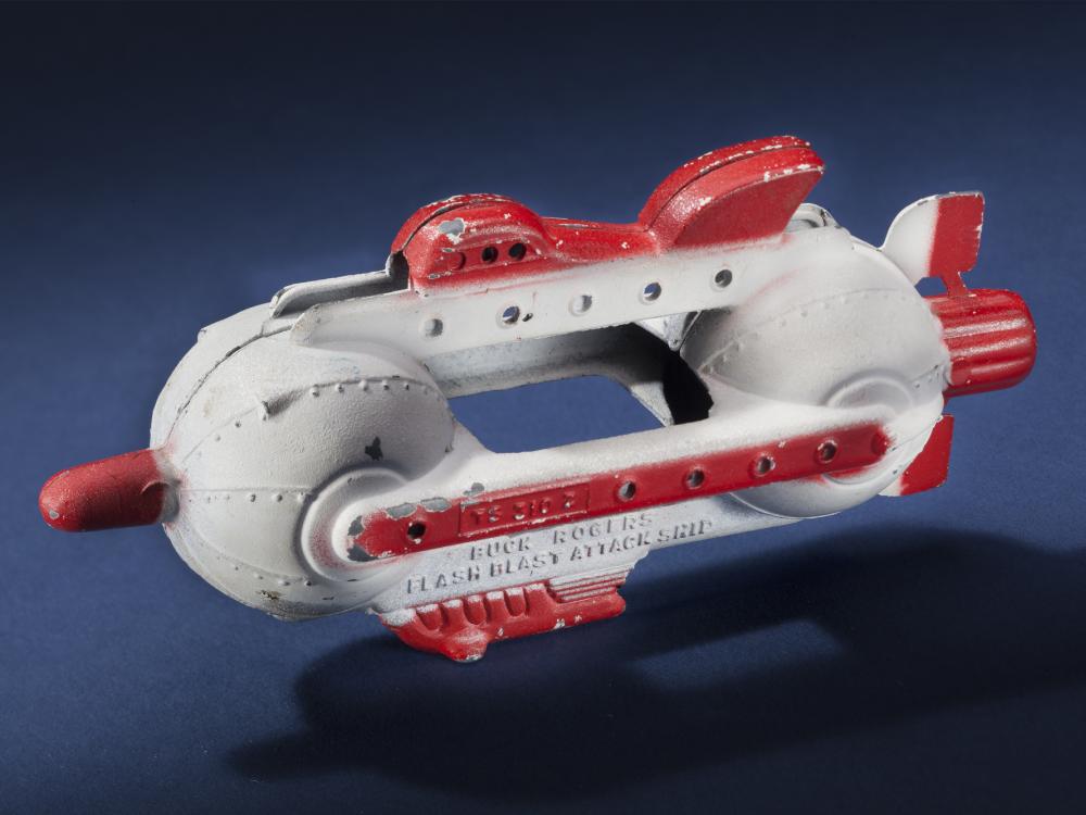 Side view of white attacking spaceship toy with center opening between two spherical sides of the ship. Ship features red fins, nose, and propellor.