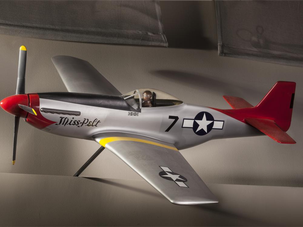 Side view of silver-colored monoplane model aircraft with one engine and a red tail and nose. Blue and white star emblem is painted on the rear of the fuselage and on the left wing.