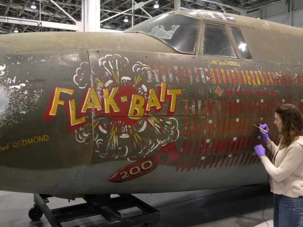 A member of the Museum's conservation staff works to conserve a portion of an olive drab green bomber aircraft from World War II.