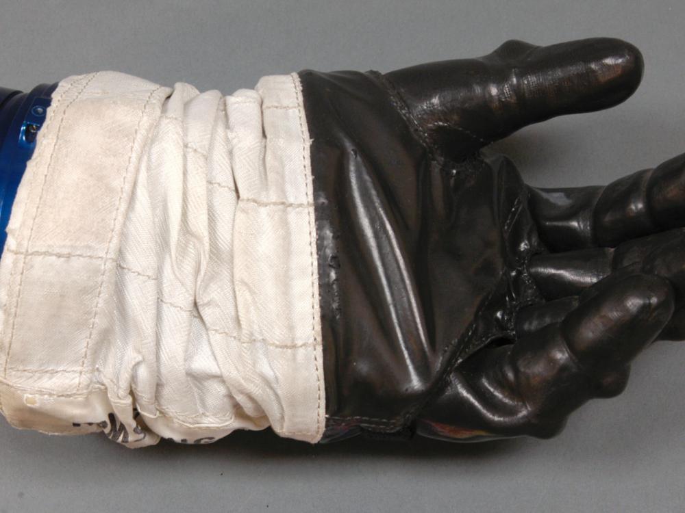 Left glove to astronaut suit. Black-colored rubber palm and fingertips section attached to a white fabric. The white fabric is attached to a solid blue disconnect from the rest of the suit.