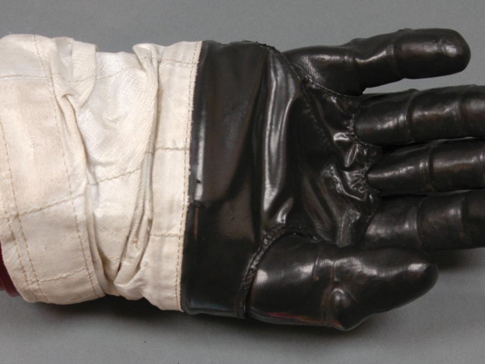 Right glove to astronaut suit. Black-colored rubber palm and fingertips section attached to a white fabric. The white fabric is attached to a solid red disconnect from the rest of the suit.