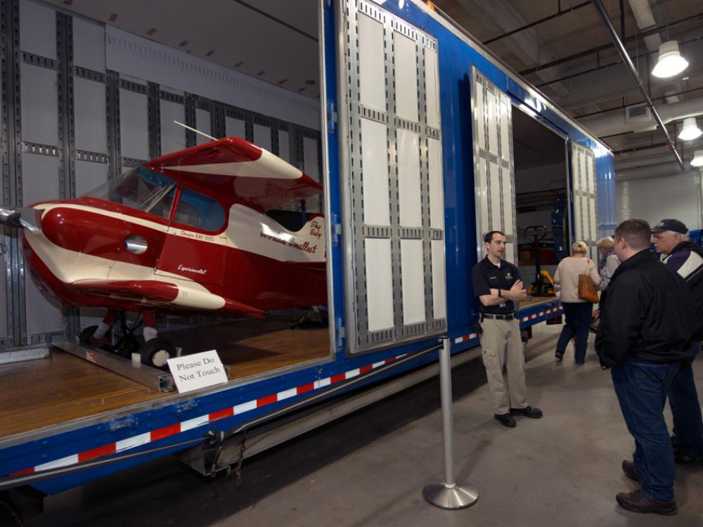 A Museum staff member provides visitors a lesson on artifact transport in front of a partially open storage unit.