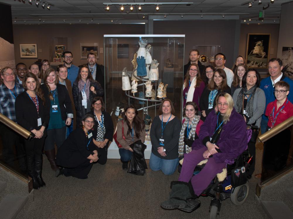 A group of people pose together around an artpiece made from various astronaut gloves.