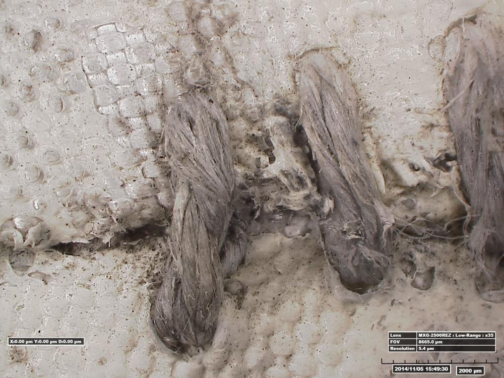 Very close-up view of three gray-colored fabric stitches which were used in the repair of a white oxygen purge system cover.