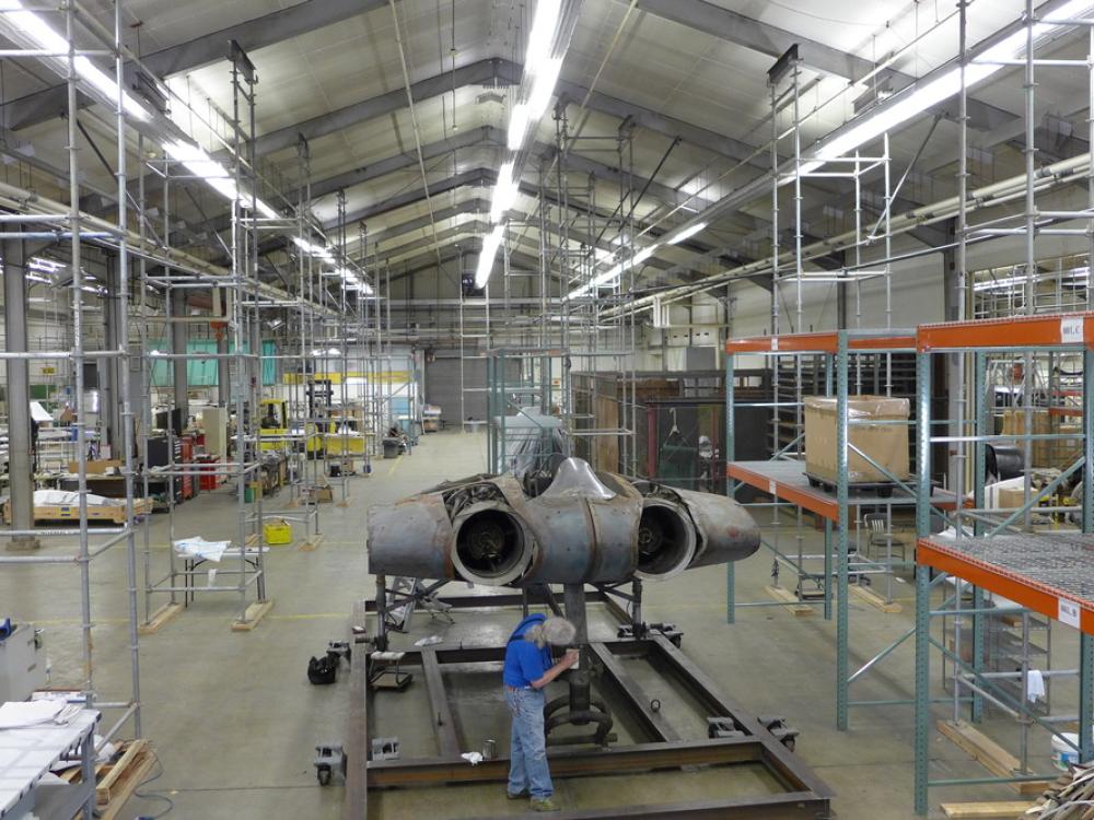 A Museum staff member is securing a gray-colored metal aircraft to a steel stand.