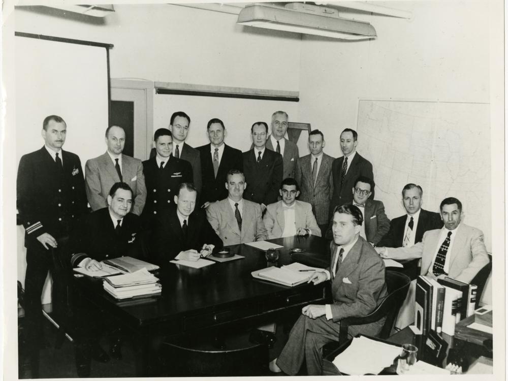 A group of men pose formally during a meeting to discuss spacecraft.