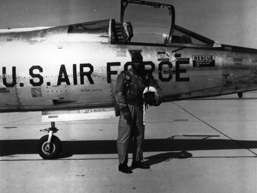 Major Robert Lawrence, an African-American male pilot and pilot, poses outside of an aircraft in aviation gear. He is holding his helmet.