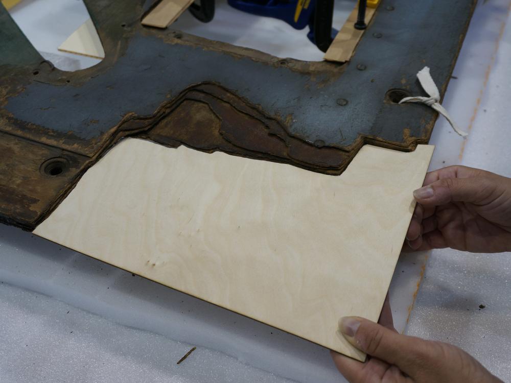 A Museum staff member holds a thin layer of plywood to be used on holes in a World War II era aircraft.