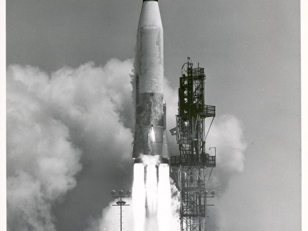 A Mercury-Atlas rocket launching from a launch pad.