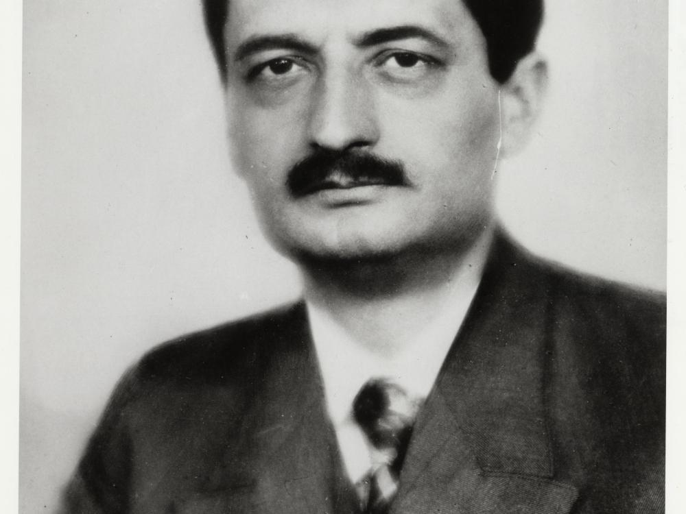 A portrait of a man with a black mustache wearing a suit.