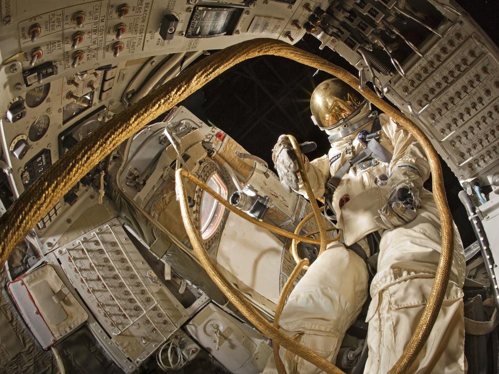 View from inside Gemini spacecraft with spacesuit emerging from the open door to visually simulate the first U.S. spacewalk.