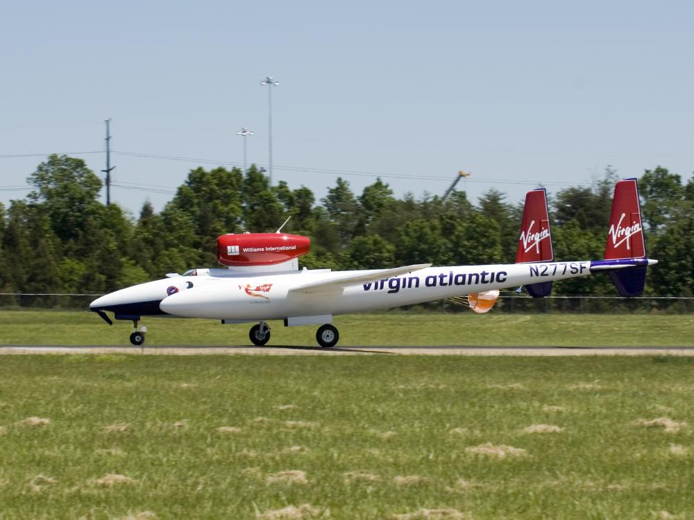 A white and red aircraft lands on a tarmac near the Udvar-Hazy Center.