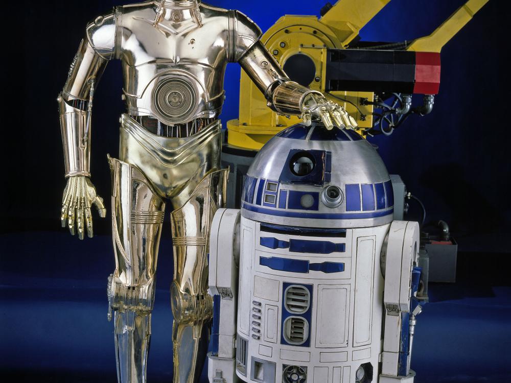 R2-D2, a blue and white robot "droid" from the Star Wars franchise, and C-3PO, a golden-metalic robot "droid" from the Star Wars franchise, stand next to each other on display at the museum.