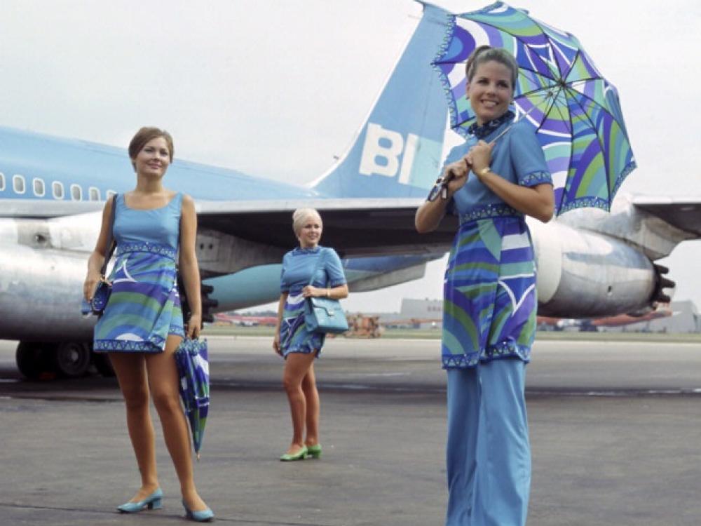 Three Braniff stewardesses posing in front of a Braniff aircraft parked on a runway.