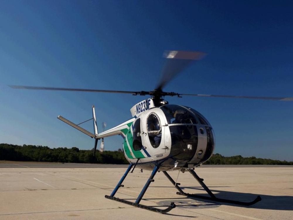 A silver and green helicopter with three propellor blades.