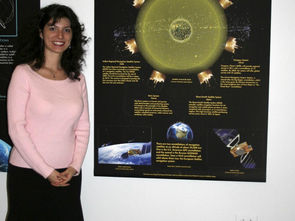 A college student stands to the side of their banner discussing social uses of GPS technology