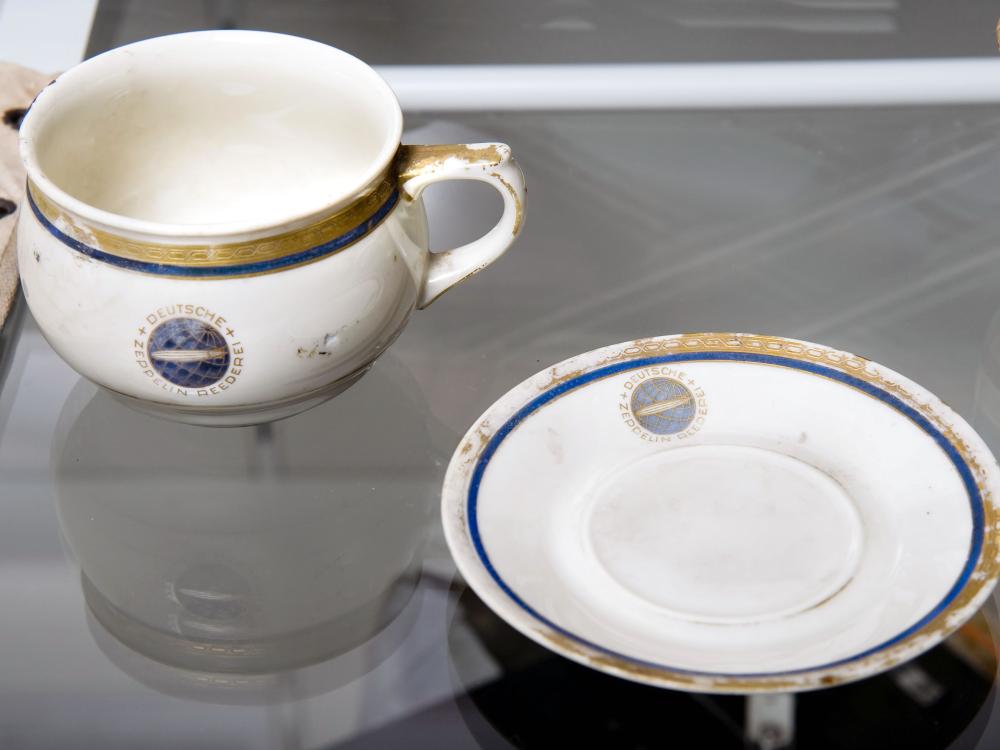 A white cup and saucer, each featuring a small depiction of the Hindenberg airship