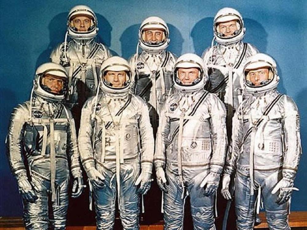 All seven Project Mercury Astronauts stand together for a photo in their space suits.