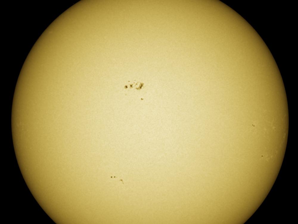 Disk view of the Sun with visible sunspot groups near the center of the Sun's visible surface.