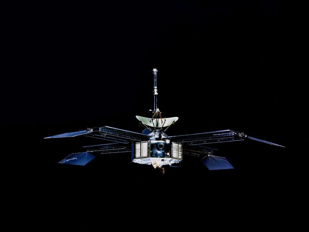 A spacecraft with a hexagonal prism-shaped base and four retractable sets of solar panels. A satellite is pointed above the base.